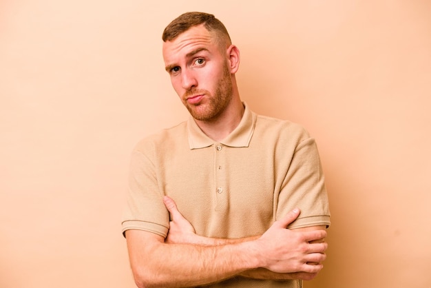 Young caucasian man isolated on beige background suspicious uncertain examining you