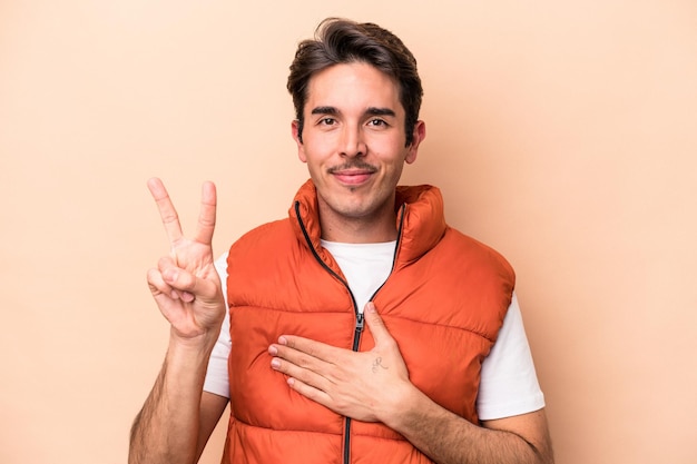 Young caucasian man isolated on beige background taking an oath putting hand on chest