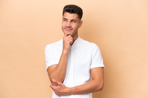 Young caucasian man isolated on beige background thinking an idea while looking up