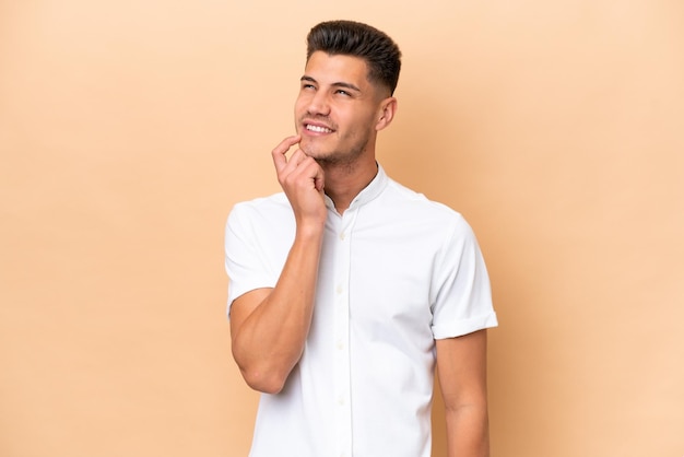 Young caucasian man isolated on beige background thinking an idea while looking up