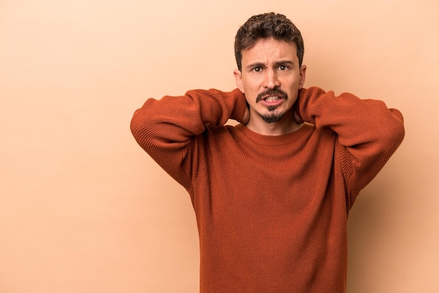 Young caucasian man isolated on beige background touching back of head, thinking and making a choice.