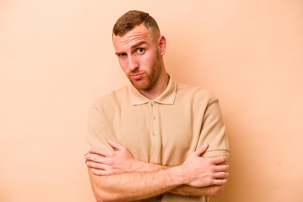 Young caucasian man isolated on beige background unhappy looking in camera with sarcastic expression