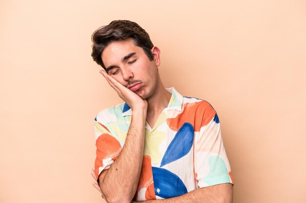 Young caucasian man isolated on beige background who is bored fatigued and need a relax day