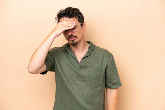 Young caucasian man isolated on beige background with headache