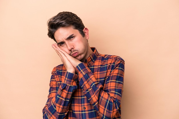 Young caucasian man isolated on beige background yawning showing a tired gesture covering mouth with hand.