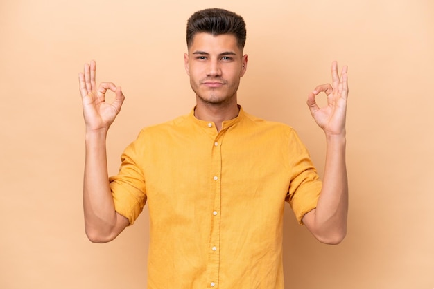 Young caucasian man isolated on beige background in zen pose