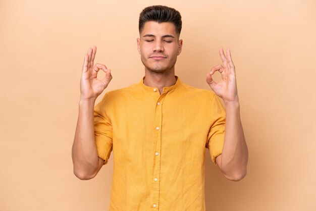 Young caucasian man isolated on beige background in zen pose