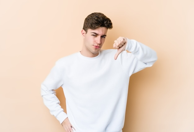 Young caucasian man isolated on beige wall showing thumb down, disappointment concept.