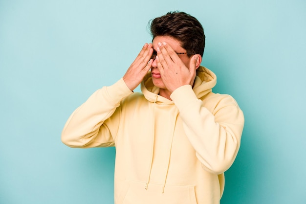 Young caucasian man isolated on blue background afraid covering eyes with hands