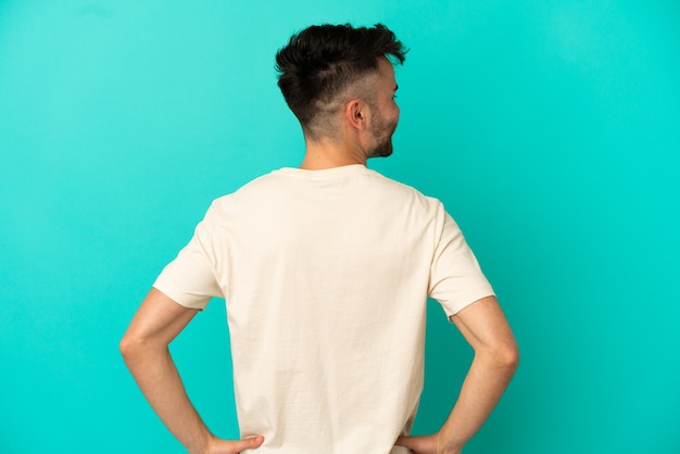 Young caucasian man isolated on blue background in back position and looking side