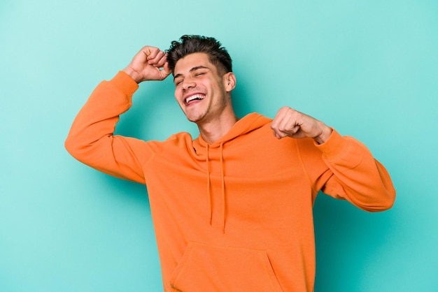 Young caucasian man isolated on blue background celebrating a special day, jumps and raise arms with energy.