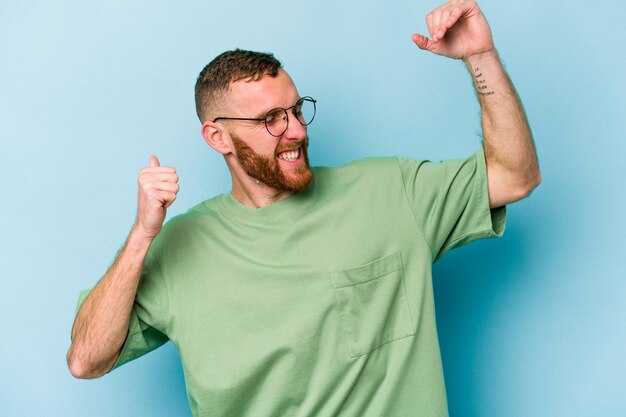 Young caucasian man isolated on blue background celebrating a special day jumps and raise arms with energy