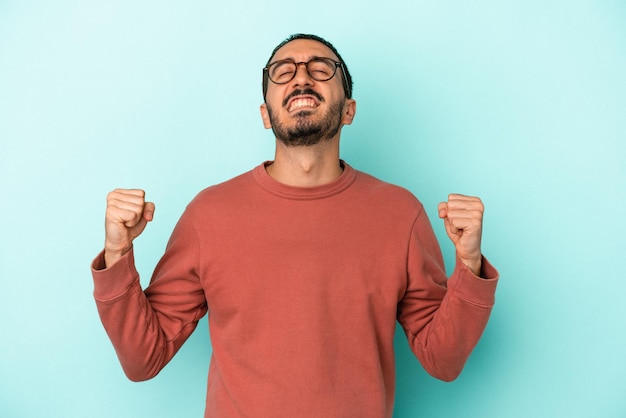 Young caucasian man isolated on blue background celebrating a victory passion and enthusiasm happy expression