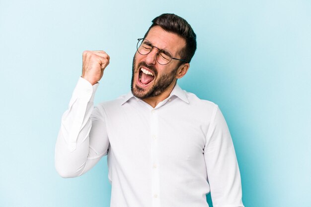 Foto giovane uomo caucasico isolato su sfondo blu che celebra un'espressione felice di passione ed entusiasmo di vittoria