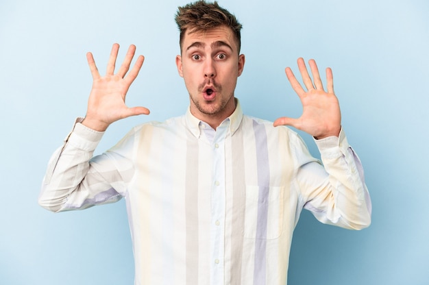 Young caucasian man isolated on blue background celebrating a victory or success, he is surprised and shocked.