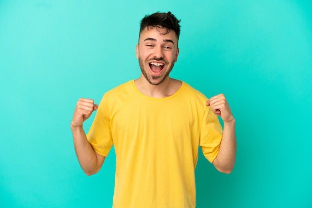 Young caucasian man isolated on blue background celebrating a victory in winner position