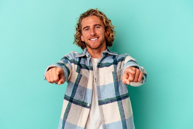 Young caucasian man isolated on blue background cheerful smiles pointing to front.