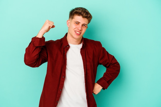 Young caucasian man isolated on blue background cheering carefree and excited. Victory concept.