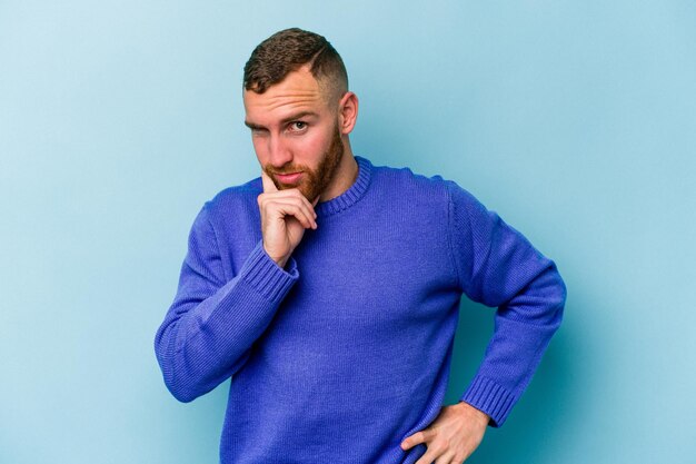 Young caucasian man isolated on blue background contemplating, planning a strategy, thinking about the way of a business.