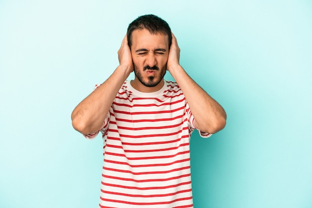 Young caucasian man isolated on blue background covering ears with hands.