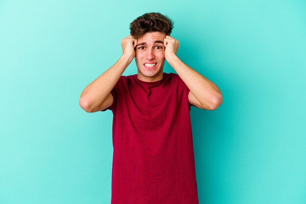 Young caucasian man isolated on blue background crying, unhappy with something, agony and confusion concept.