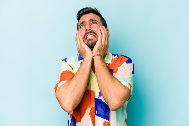 Young caucasian man isolated on blue background crying unhappy with something agony and confusion concept