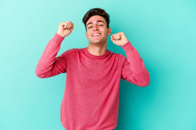 Young caucasian man isolated on blue background dancing and having fun.