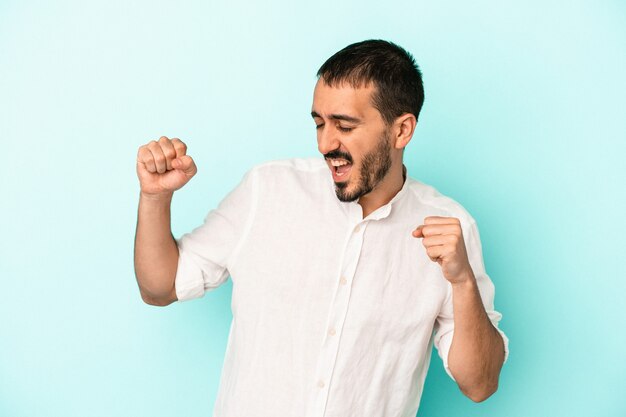 Young caucasian man isolated on blue background dancing and having fun.