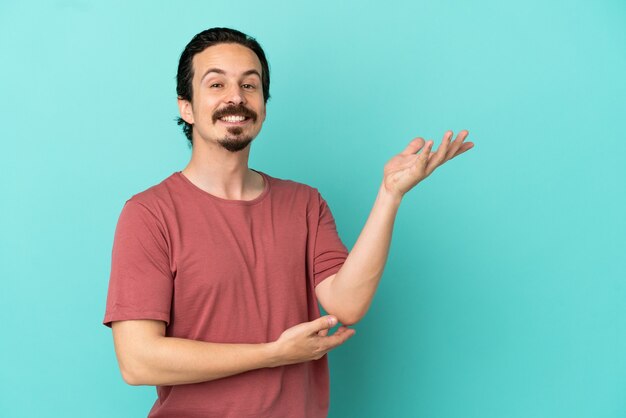 Young caucasian man isolated on blue background extending hands to the side for inviting to come