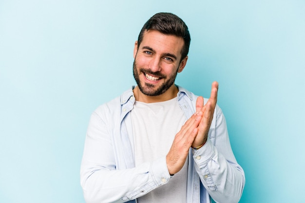 Young caucasian man isolated on blue background feeling energetic and comfortable rubbing hands confident