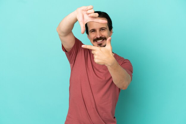 Young caucasian man isolated on blue background focusing face. Framing symbol