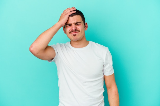 Young caucasian man isolated on blue background forgetting something, slapping forehead with palm and closing eyes.