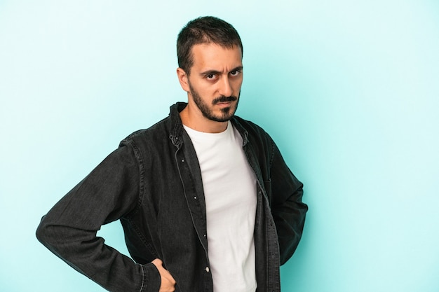 Young caucasian man isolated on blue background frowning face in displeasure, keeps arms folded.