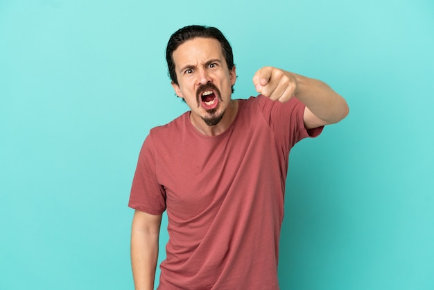 Young caucasian man isolated on blue background frustrated and pointing to the front