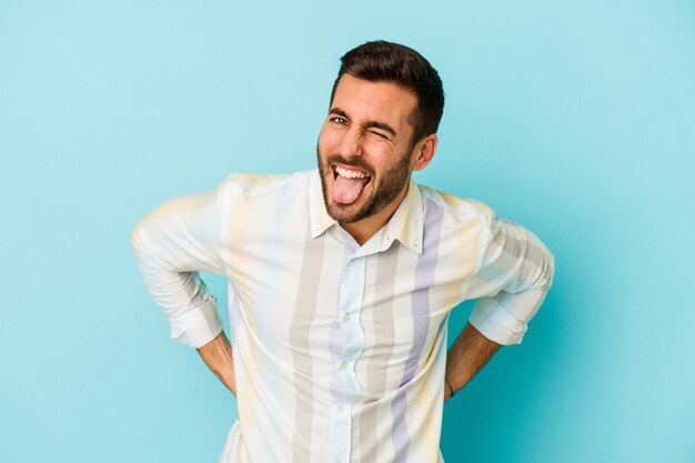 Young caucasian man isolated on blue background funny and friendly sticking out tongue.