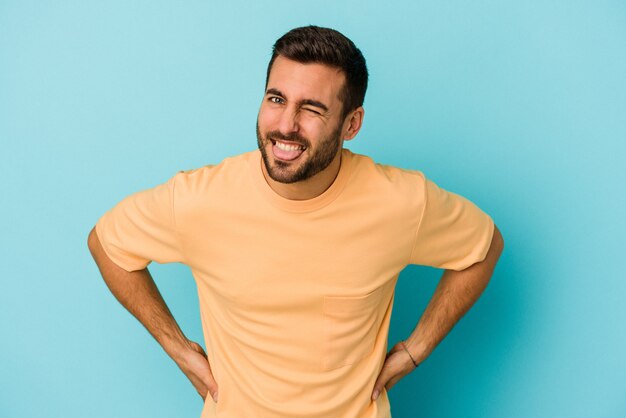 Young caucasian man isolated on blue background funny and friendly sticking out tongue.