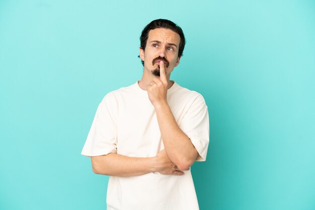 Young caucasian man isolated on blue background having doubts while looking up