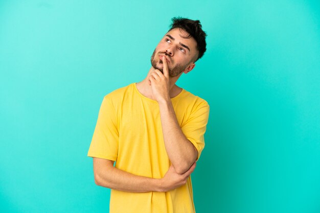 Young caucasian man isolated on blue background having doubts while looking up