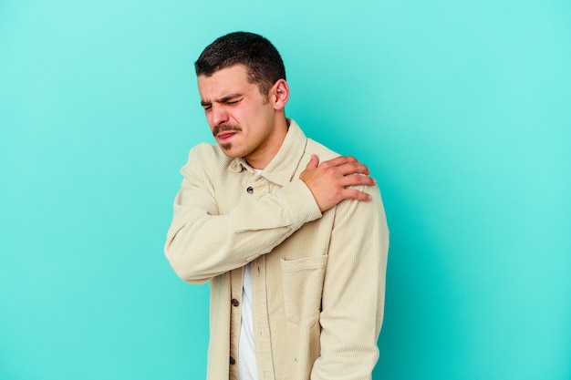 Young caucasian man isolated on blue background having a shoulder pain.