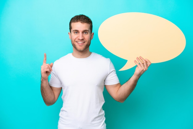 Young caucasian man isolated on blue background holding an empty speech bubble with surprised expression