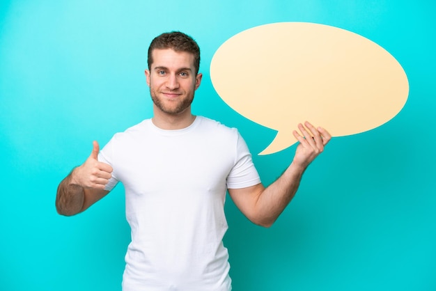 Young caucasian man isolated on blue background holding an empty speech bubble with thumb up