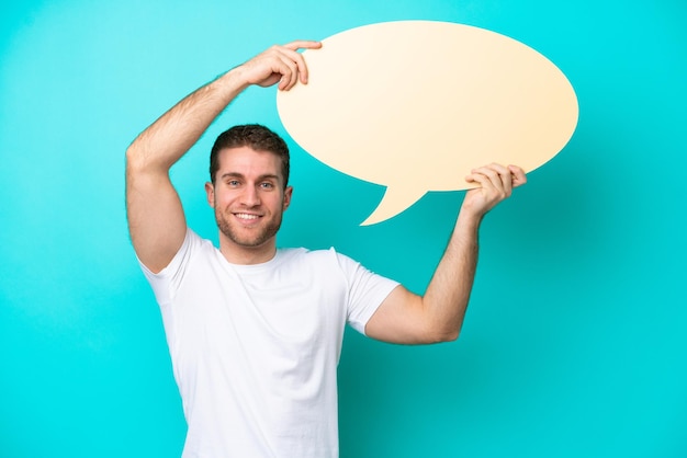 Young caucasian man isolated on blue background holding an empty speech bubble
