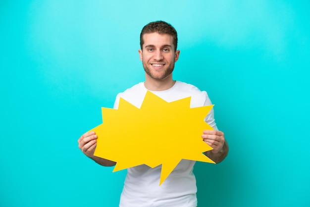 Young caucasian man isolated on blue background holding an empty speech bubble