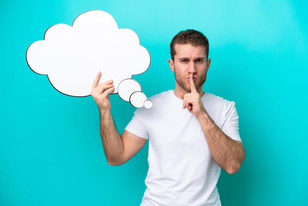 Young caucasian man isolated on blue background holding a thinking speech bubble and doing silence gesture