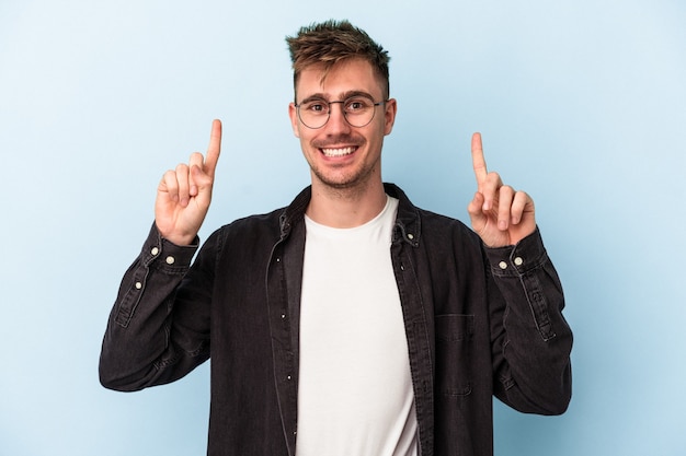 Young caucasian man isolated on blue background indicates with both fore fingers up showing a blank space.