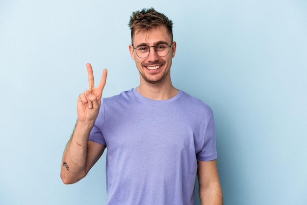 Young caucasian man isolated on blue background joyful and carefree showing a peace symbol with fingers.