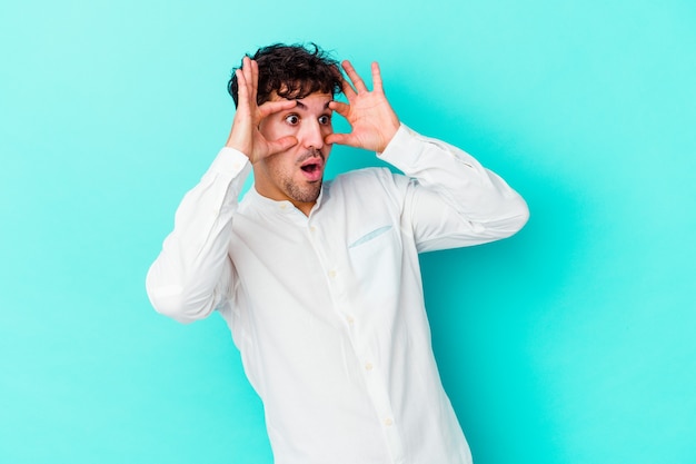 Young caucasian man isolated on blue background keeping eyes opened to find a success opportunity.