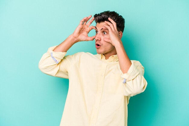 Photo young caucasian man isolated on blue background keeping eyes opened to find a success opportunity.