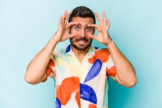 Young caucasian man isolated on blue background keeping eyes opened to find a success opportunity