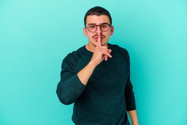 Young caucasian man isolated on blue background keeping a secret or asking for silence.